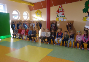 Grupa dzieci siedzi na krzesłach, słuchają dzieci recytujących wiersze, które uczestniczą w konkursie.